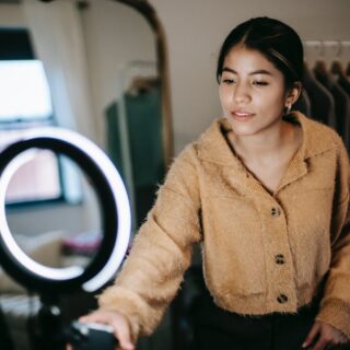 ethnic female blogger filming video on cellphone with light lamp