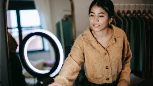 ethnic female blogger filming video on cellphone with light lamp