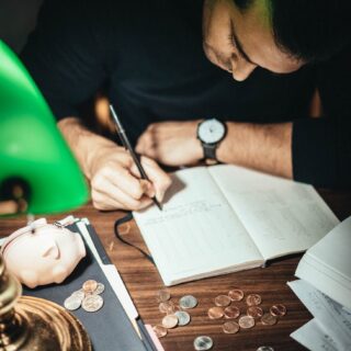 crop accountant taking notes at desk with scattered coins