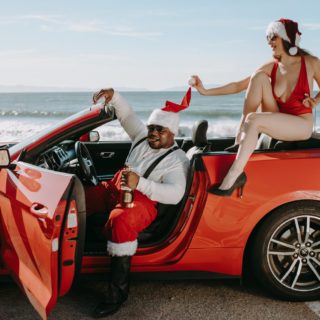 man and woman in santa outfits sitting in a red convertible car