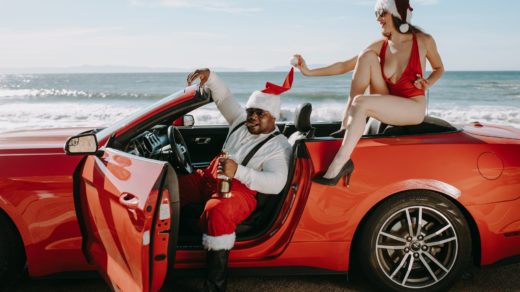 man and woman in santa outfits sitting in a red convertible car
