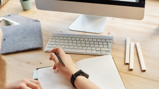 person using silver imac while holding pencil