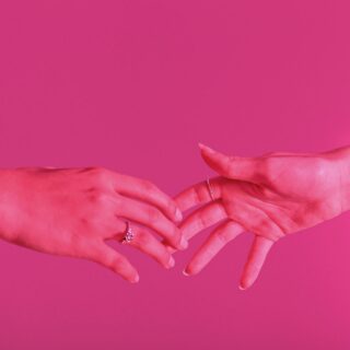 photo of hands touching against pink background